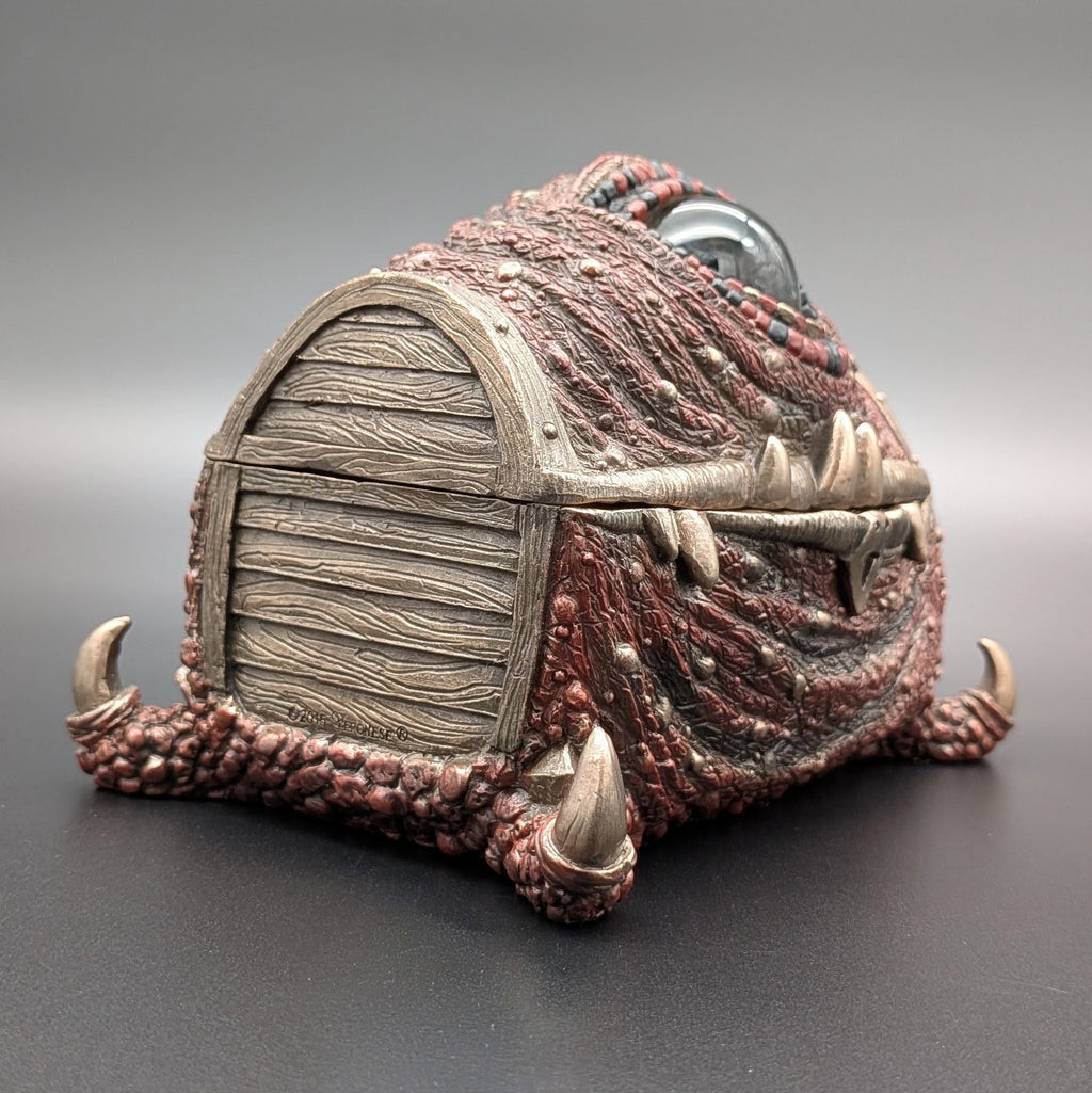 A fantasy miniature chest designed to look like a monster's scaly skin with a wood effect end, photographed on a dark gray gradient background.