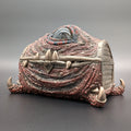 A fantasy creature-themed storage chest with textured red and brown scales, spikes, claw-like feet, and an eye on top, photographed on a dark gray studio background.