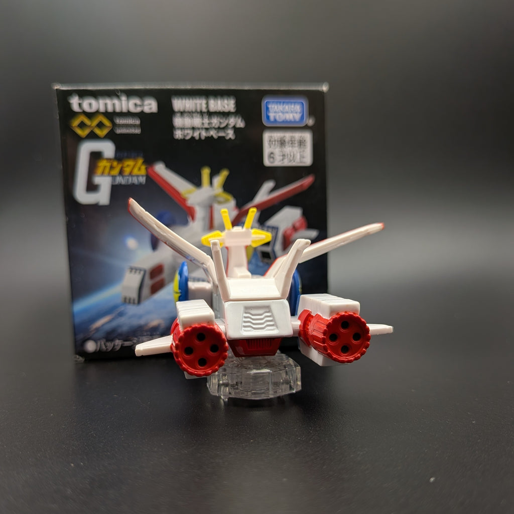 A Tomica Gundam White Base model  toy with its original packaging box, displayed on a dark gray surface.