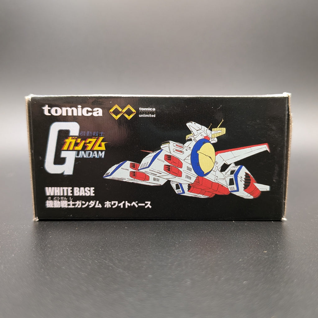 Tomica Gundam White Base  packaging box, featuring a black background with white, red, and blue Gundam illustrations and Japanese text.