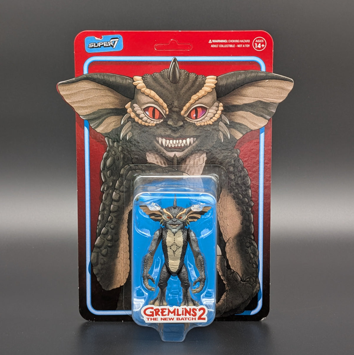 Super7 Gremlins 2 The New Batch action figure in its original blister card packaging, featuring a large grey and brown gremlin face on the backing card and a smaller figure in a blue blister pack in front.