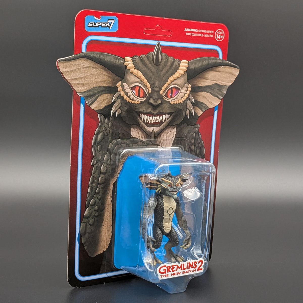 Super7 Gremlins 2 The New Match action figure in its original retro-style blister card packaging, featuring a large red and blue card with a detailed Gremlin face illustration.