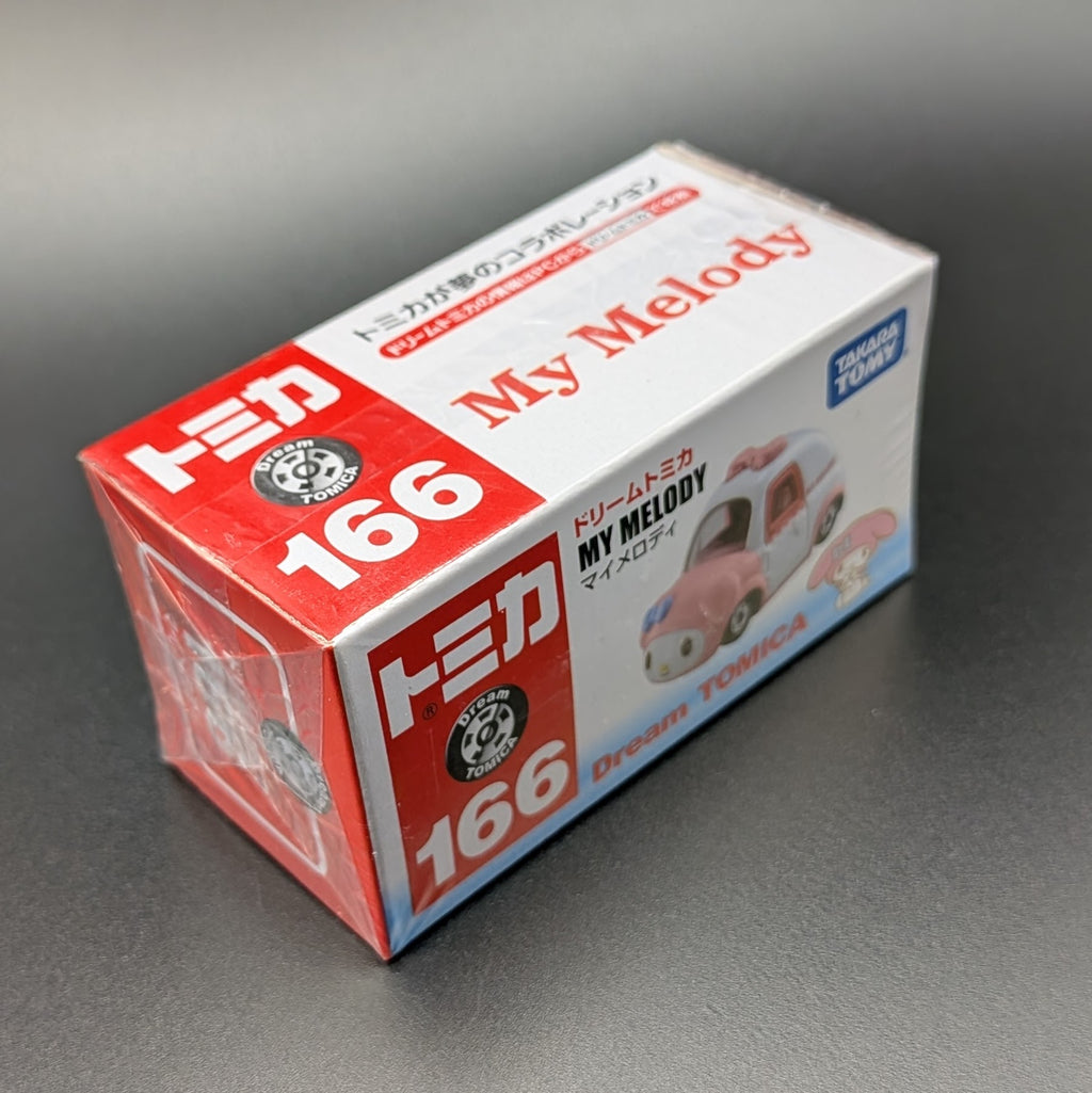 A boxed Tomica My Melody Dream car package photographed on a dark gray studio surface. The box is white with large red '166' panels and red 'My Melody' text, plus a small blue Tomy logo and an illustration of the pink car.