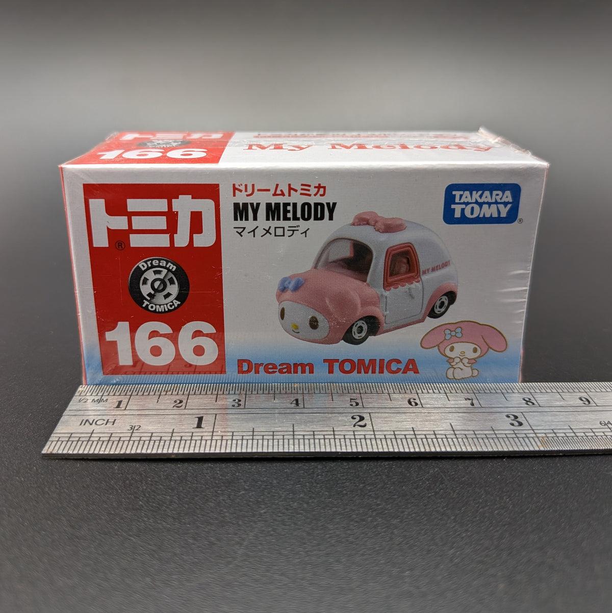 A boxed Takara Tomica Dream Tomica My Melody model car set, shown in its original retail packaging with a metal ruler in front for scale on a gray surface.