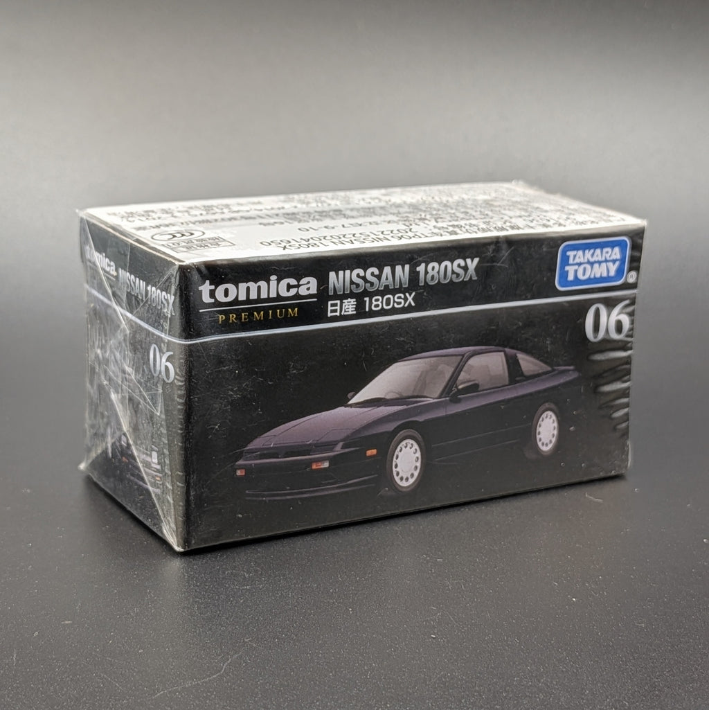A boxed Tomica Nissan 180SX model car package on a dark gray background. The box is mostly black with white text and a printed photo of a  coupe car.