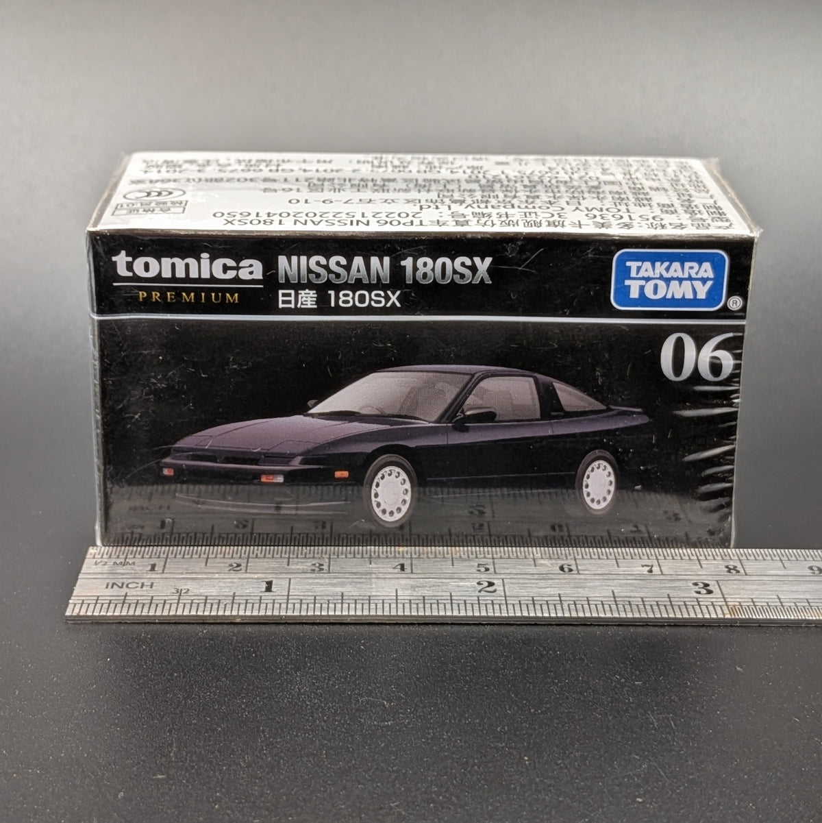 Tomica Premium Takara Tomy Nissan 180SX model car box, number 06, shown with a metal ruler in front on a dark gray background.