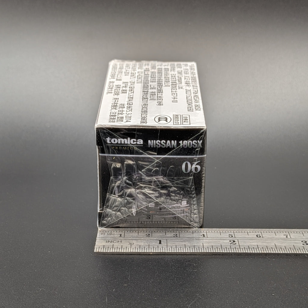 A boxed model train accessory labeled tomica NISSAN 180SX 06, shown on a dark surface with a metal ruler along the bottom edge for scale.