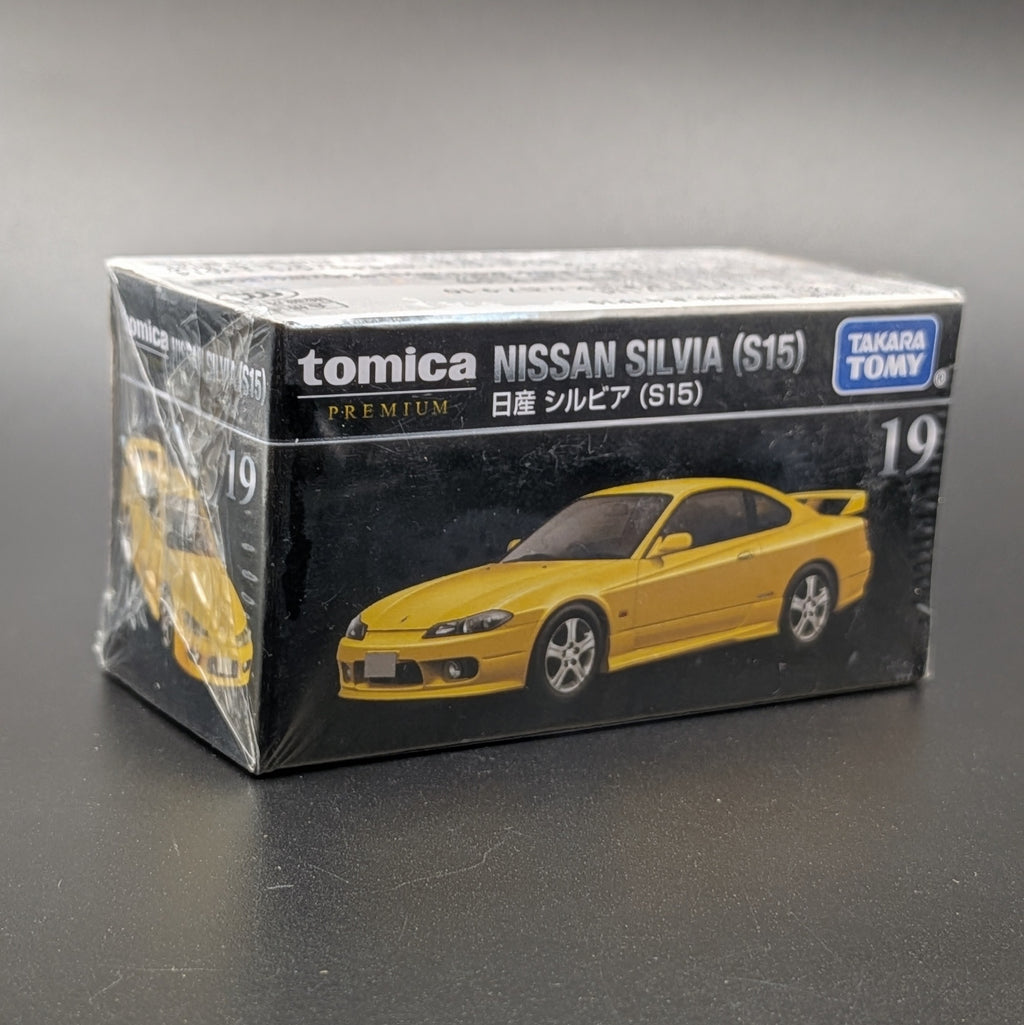 A boxed Tomica Nissan Silvia (S15) model car set, still wrapped in clear plastic, on a dark gray surface. The box is black with white text and shows a yellow car graphic, with the Takara Tomy logo in the top right.