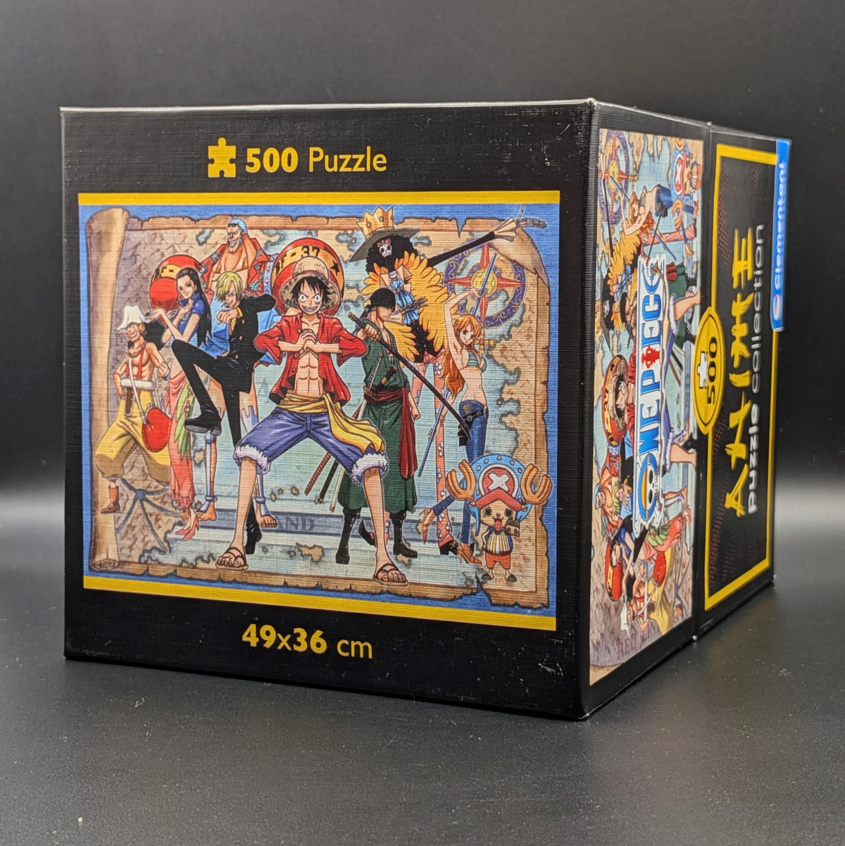 One Piece Straw Hat Crew 500pc puzzle still sealed in Clementoni's signature square box. The box features a detailed, colourful illustration of Luffy, Nami, Zoro and the crew. Shown at 3/4 view angle, displayed on a dark grey background.