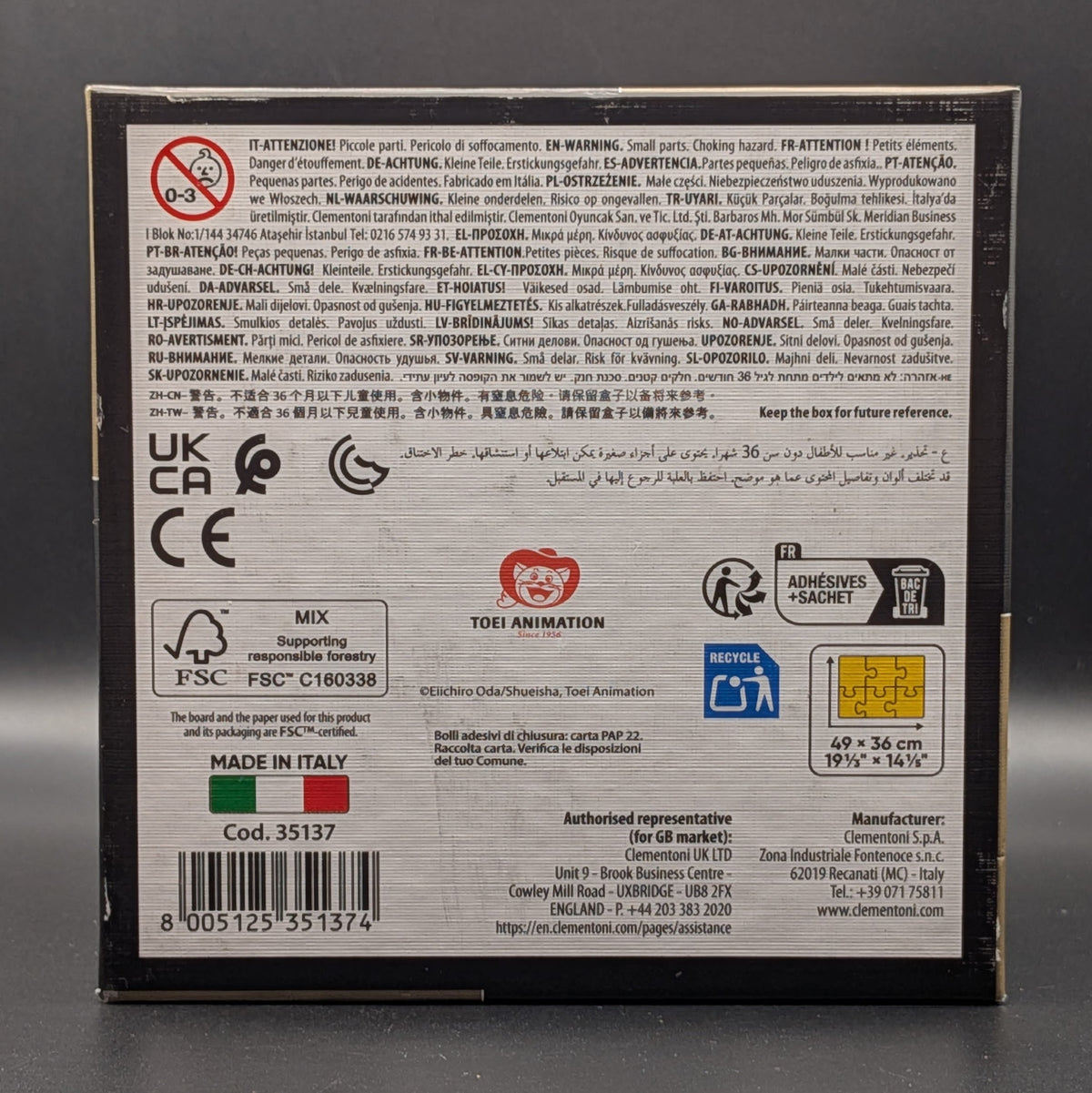 One Piece Straw Hat Crew puzzle still sealed in Clementoni's signature square box. The box features a detailed, colourful illustration of Luffy, Nami, Zoro and the crew. Showing the base with the additional information and barcode, displayed on a dark grey background.