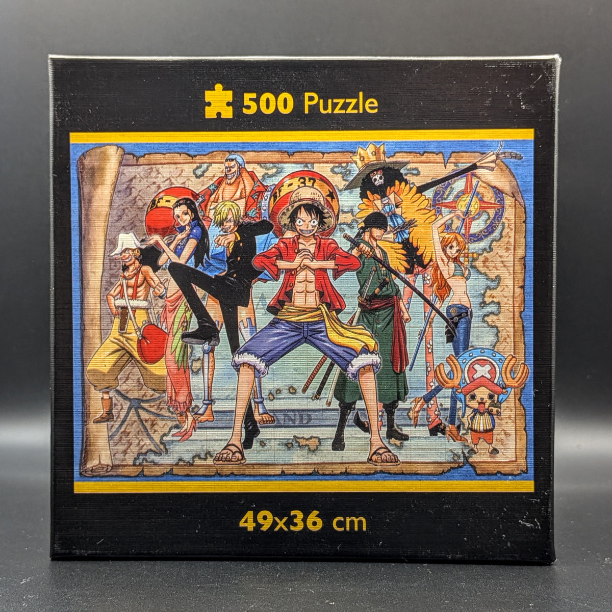One Piece Straw Hat Crew 500pc puzzle still sealed in Clementoni's signature square box. The box features a detailed, colourful illustration of Luffy, Nami, Zoro and the crew. Showing the finished puzzle image when complete, displayed on a dark grey background.