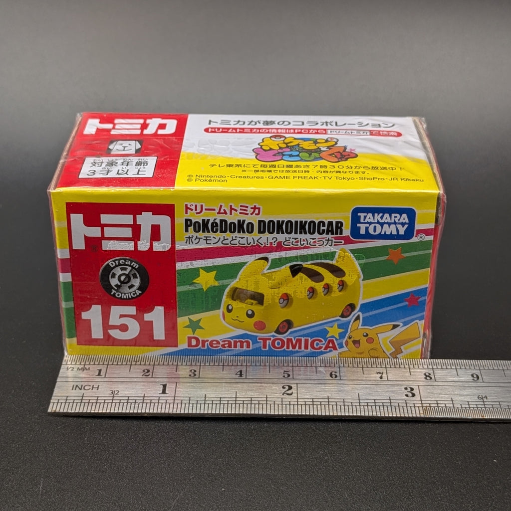 a boxed PoKéDoKo Dokoikocar by Takara Tomy can be seen in its packaging, on a textured grey background. Shown against a metal ruler for scale. 