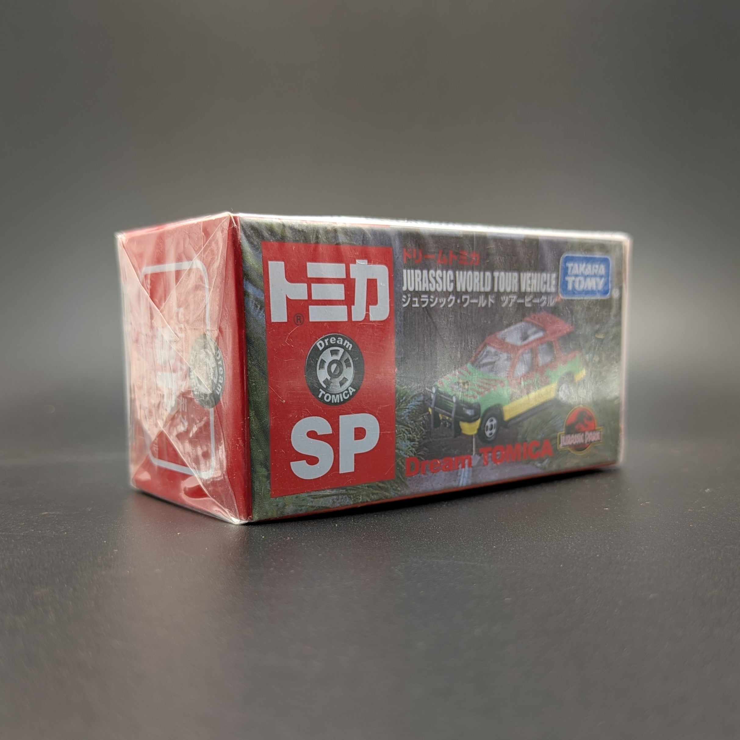 Takara Tomy Dream Tomica SP Jurassic World Tour Vehicle (Ford Explorer), 1/64 scale diecast boxed and unopened. The box is at a 3/4 view facing to the right and displayed on a black background.