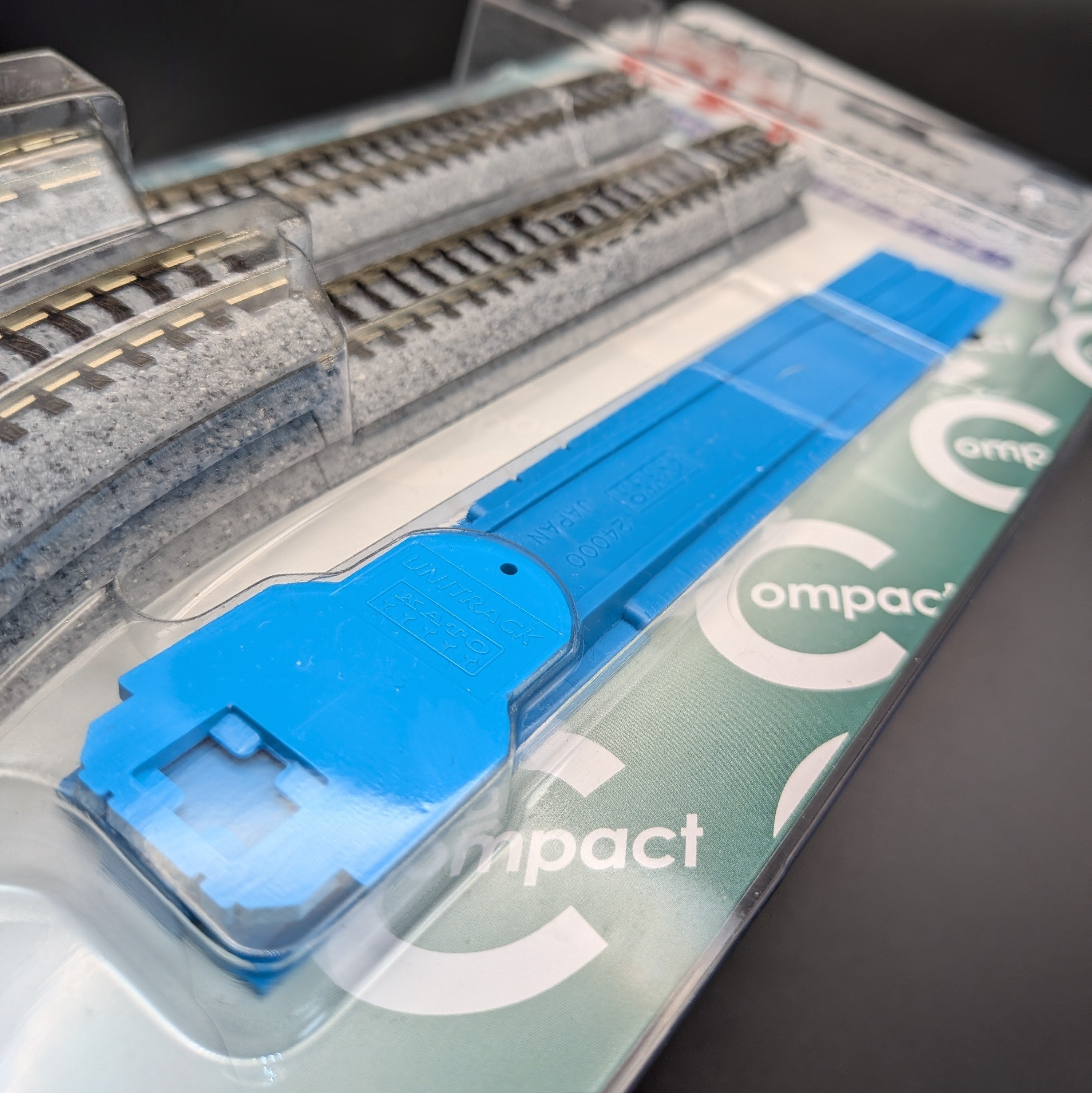 Kato CV1 Unitrack Compact Endless
 Track Set (model 20-890) in its original packaging, featuring a close up of some of the parts to make a complete oval track and sat on a black background.