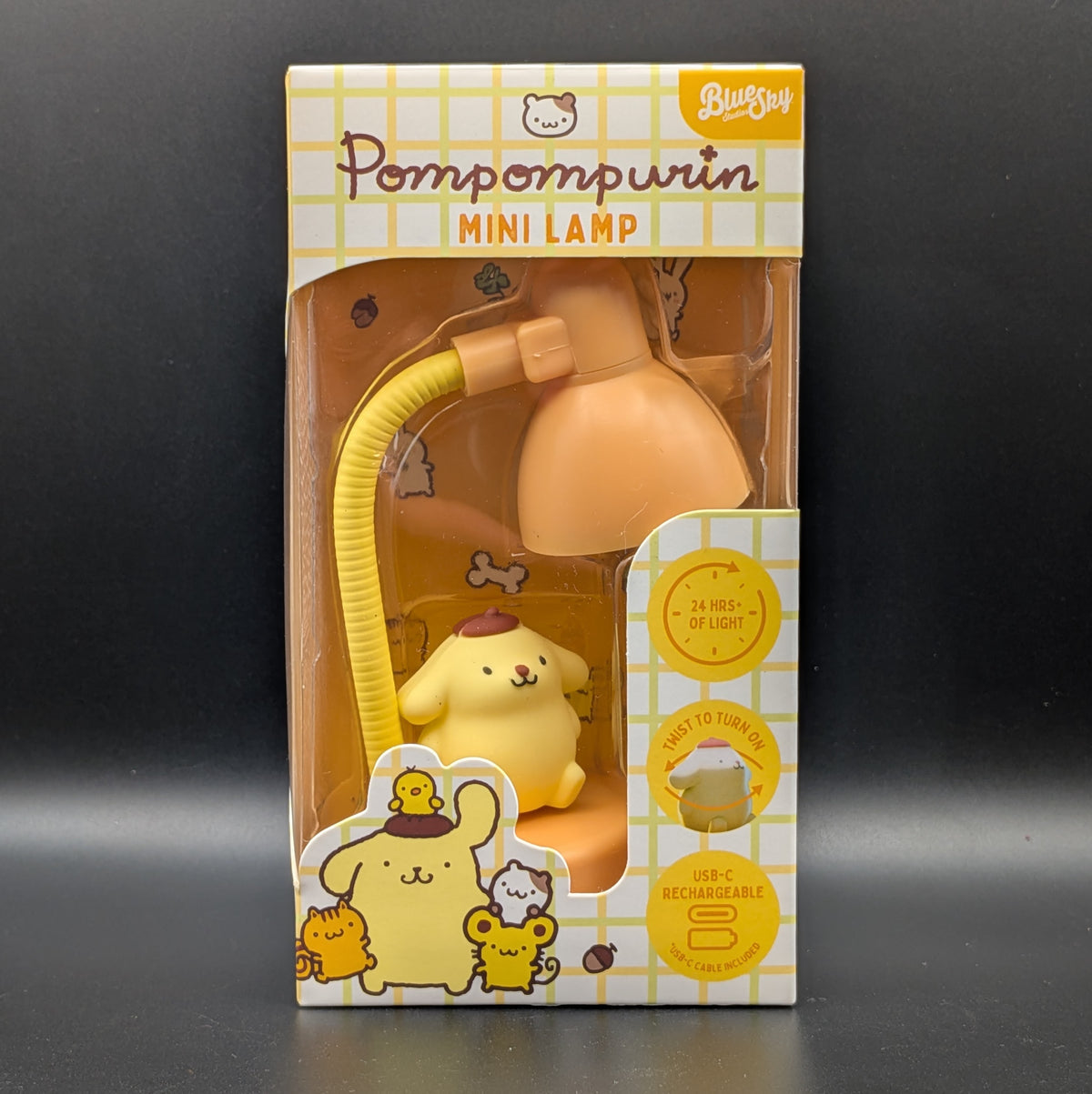 Pompompurin mini desk lamp in its original retail packaging, featuring a yellow character lamp and a flexible yellow cord under a peach-colored shade, with a white and yellow grid-patterned box.
