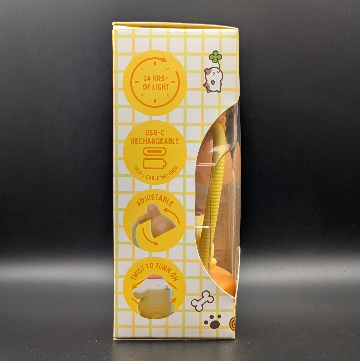 A boxed accessory shown upright on a dark studio background. The package is mostly white with a yellow grid pattern and large yellow circular callout graphics on the front, with a clear window revealing a yellow product inside.