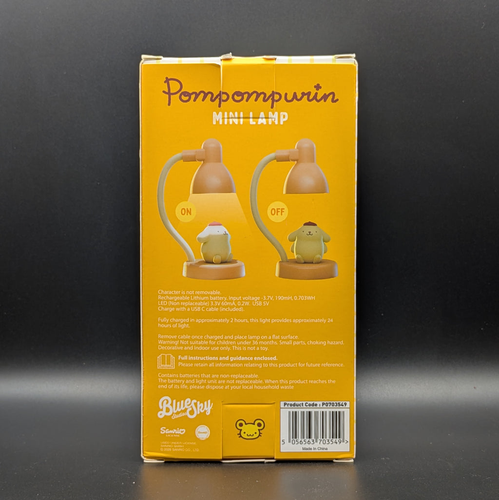 The back of a yellow Pompompurin Mini Lamp product box, showing illustrations of the lamp and product details, photographed against a dark gray background.
