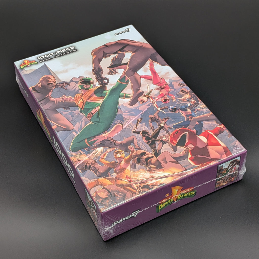 A boxed jigsaw puzzle featuring Power Rangers artwork, photographed on a dark gray studio background. The box is wrapped in clear plastic and shows the Power Rangers logo on the front and side.