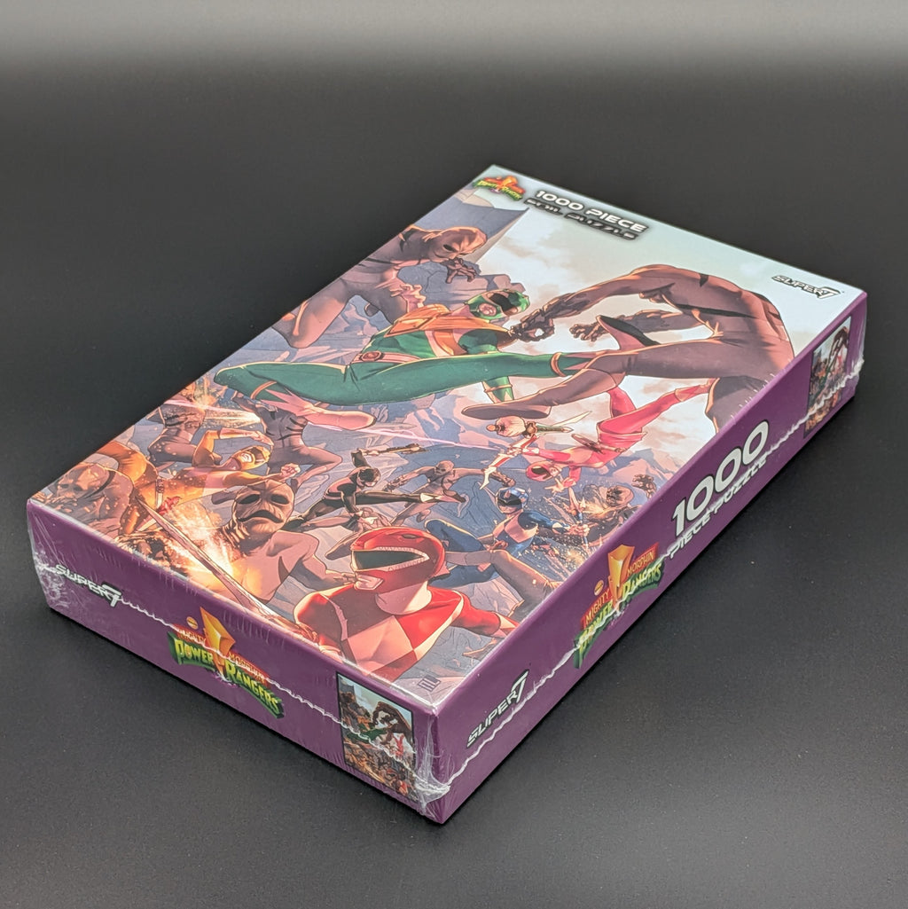 A 1000-piece Power Rangers jigsaw puzzle box from Super7, sealed in plastic wrap, set against a dark gray background. The box features a colorful illustration of the Power Rangers team and has a purple base color.
