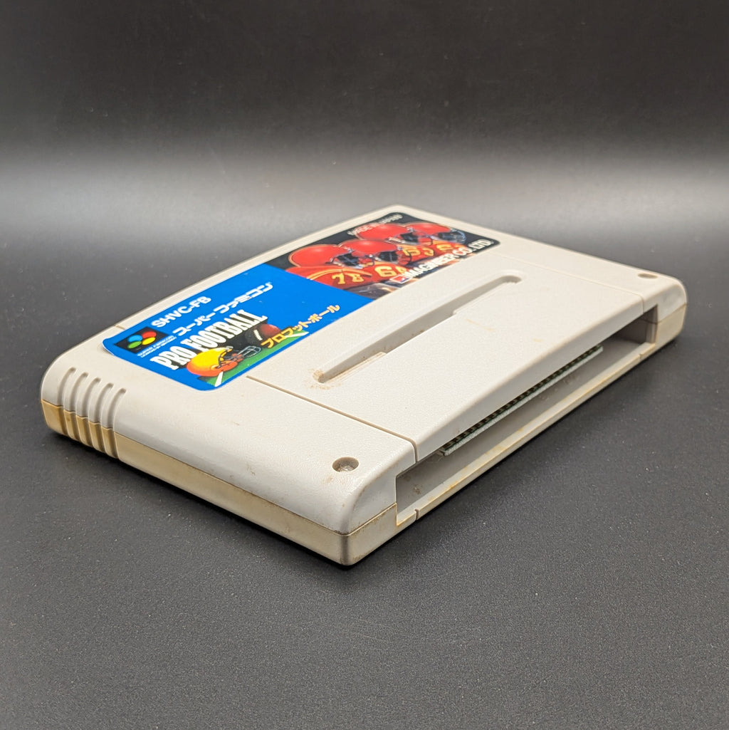 Pro Football (SHVC-FB) video game cartridge for the Super Famicom Entertainment System, shown laying on its back with the label facing up, at a 3/4 angle. Pictured on a dark grey background.