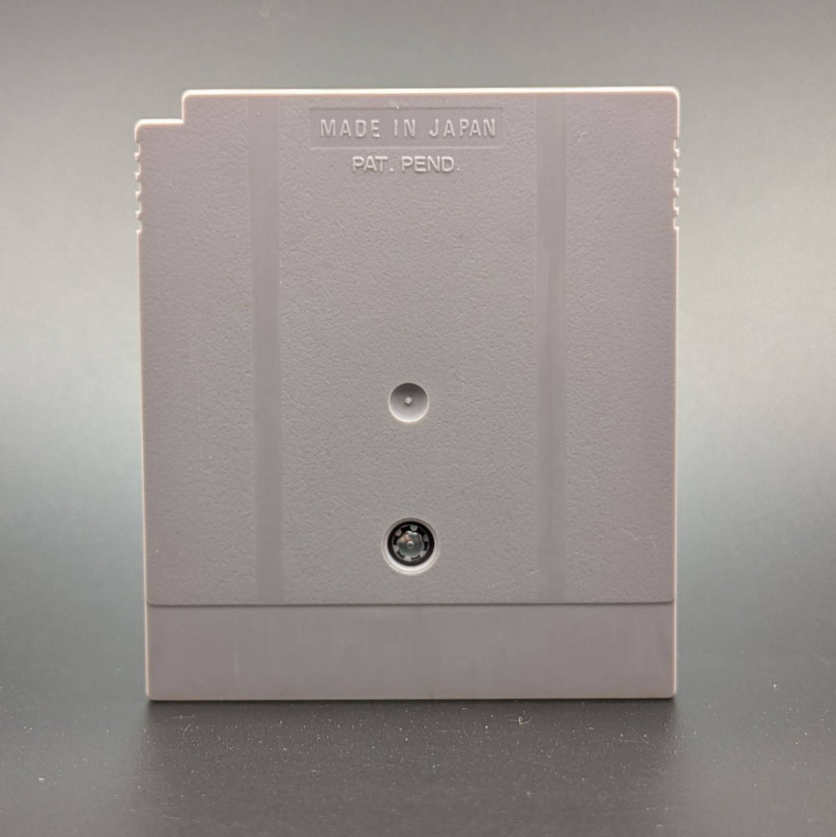 Reverse of a Game Boy Cartridge on a textured surface, featuring the embossed text 'MADE IN JAPAN PAT. PEND.