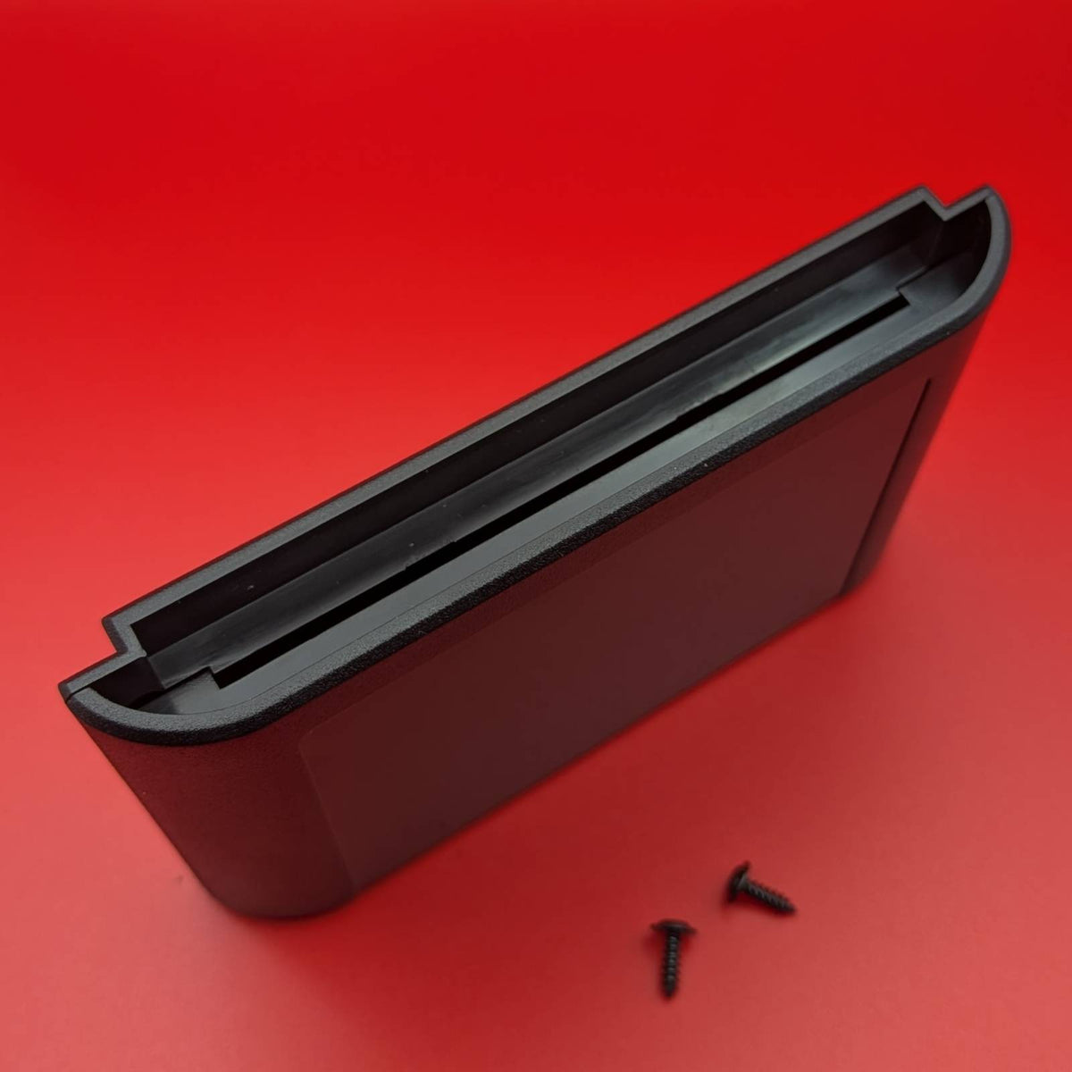 A black plastic video game cartridge shown bottom up on a solid red background with two small black screws.