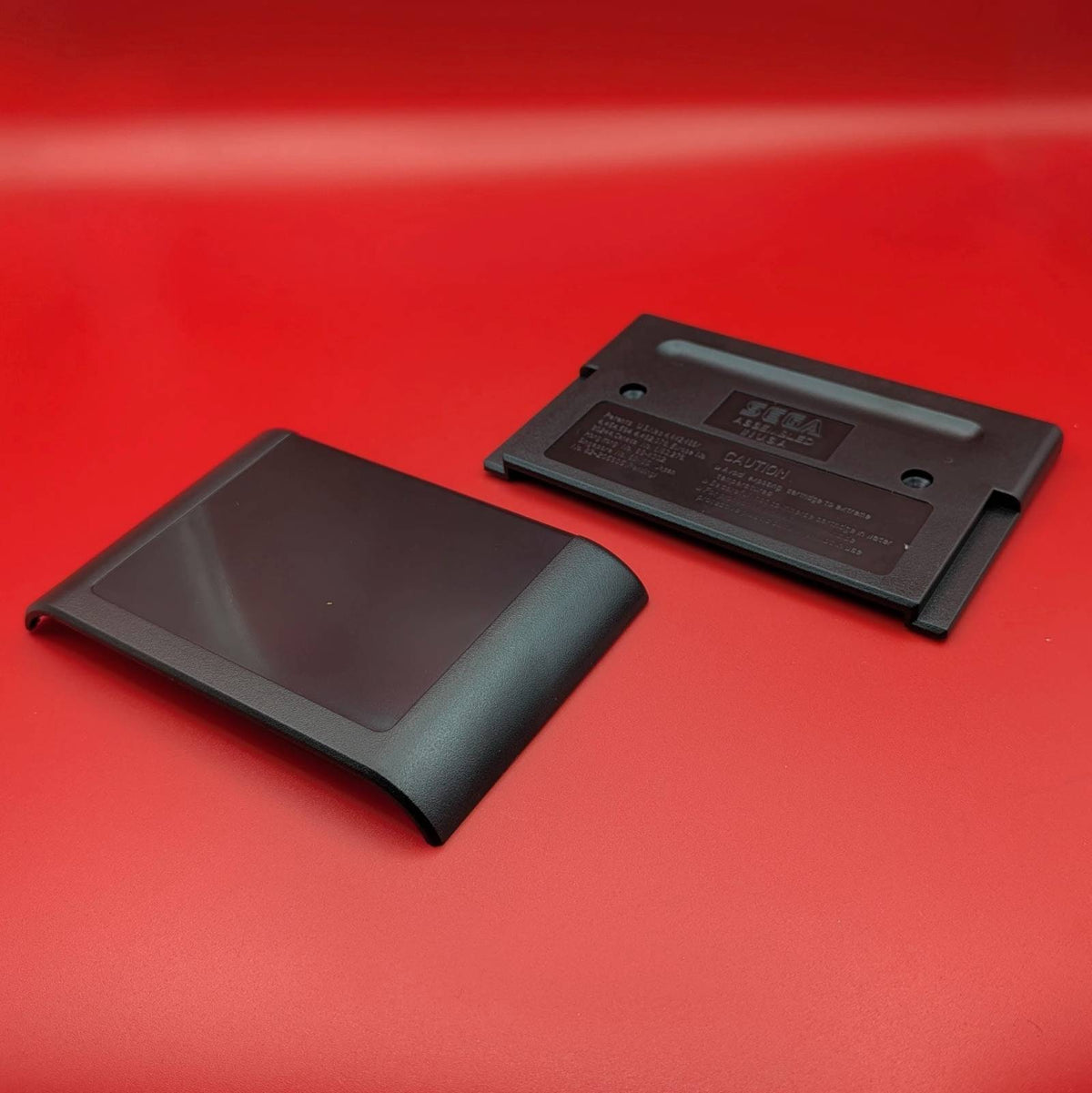 Two black plastic replacement parts, cartridge front and a back plate, displayed on a solid red backgrounnd.