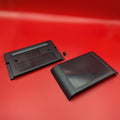 A black plastic replacement cover for a game cartridge, shown in two pieces: the back plate with embossed text and a small screws, and the front cover with a glossy black panel, displayed on a red background.