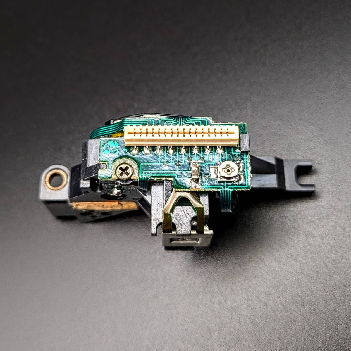 A replacement electronic connector module with a green circuit board, gold-plated pins, and black plastic housing, photographed on a dark gray background.