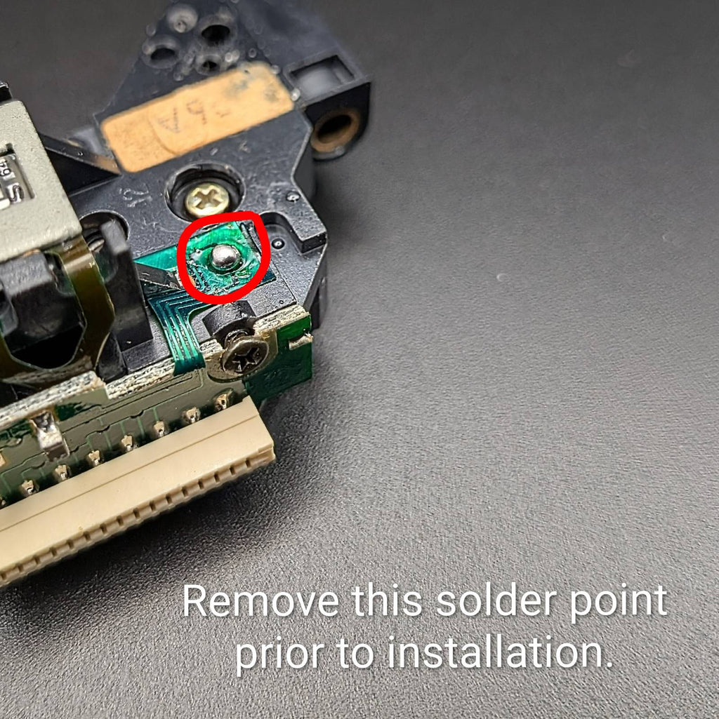 Close-up of an electronic component on a dark textured surface, with a red circle highlighting a specific solder point and text reading 'Remove this solder point prior to installation.'.