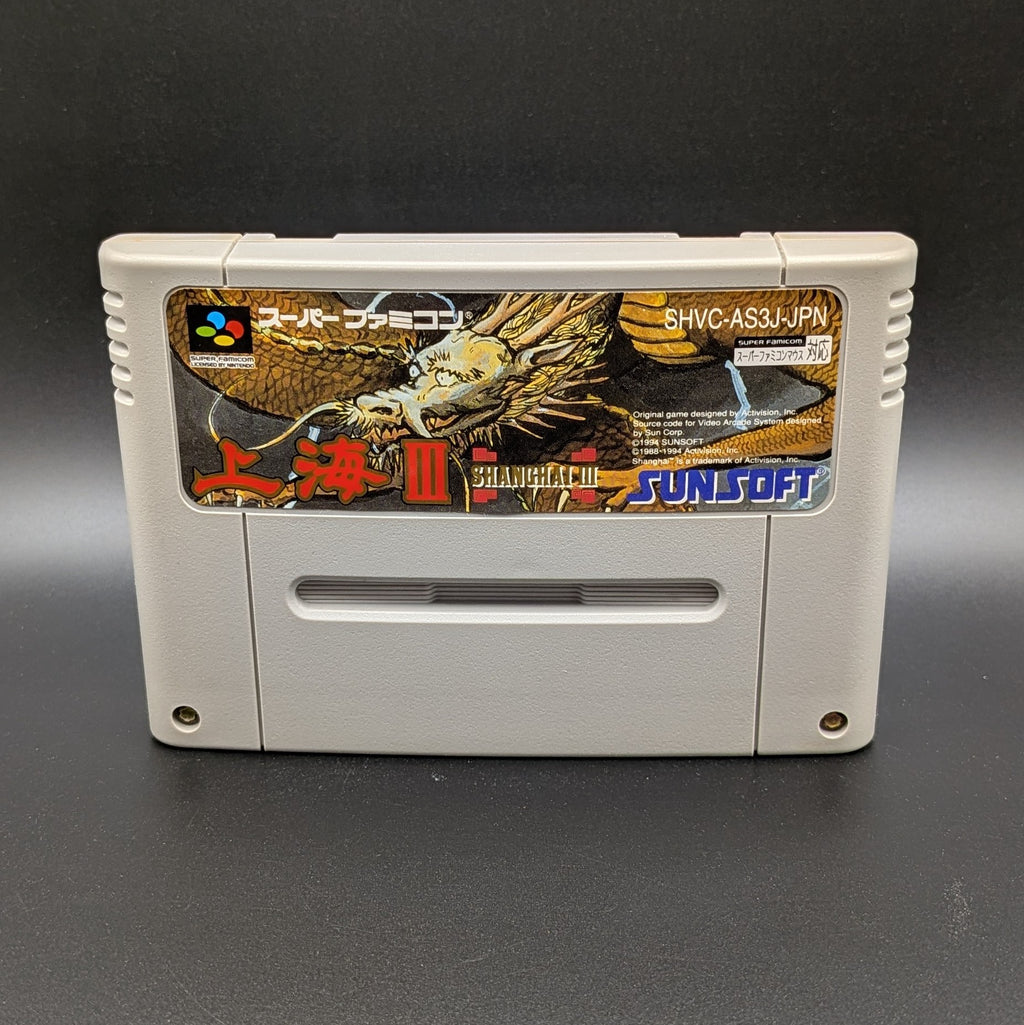 Shanghai 3 video game cartridge for Nintendo's Super Famicom (SFC) Entertainment System, shown standing up and facing forwards on a dark grey background.