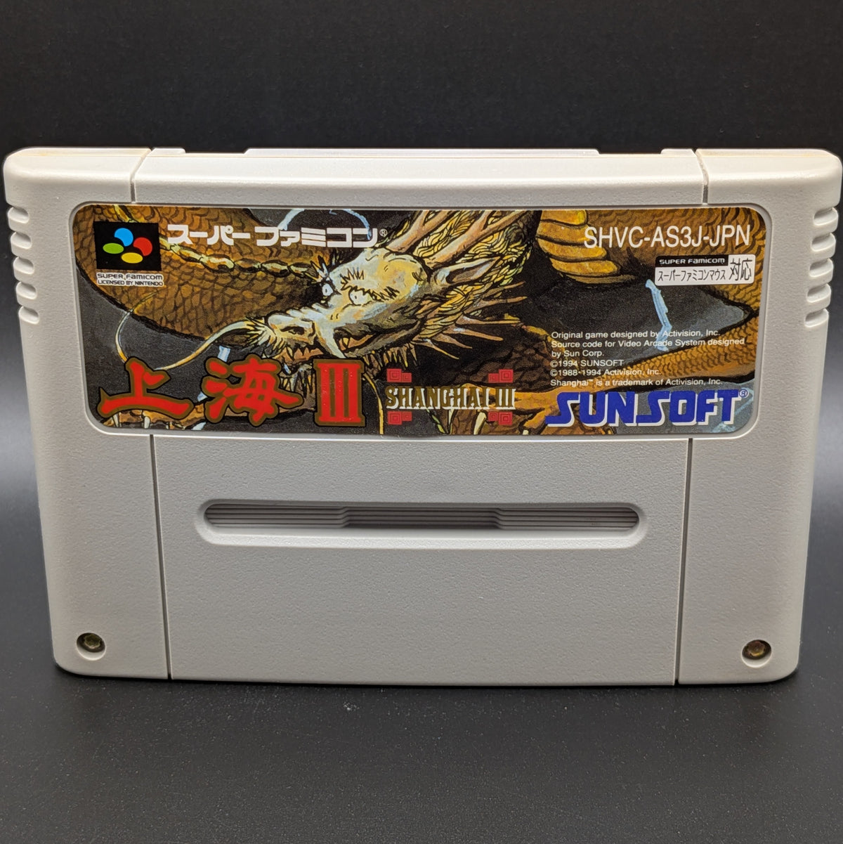 A close up of Shanghai 3 video game cartridge for Nintendo's Super Famicom (SFC) Entertainment System, shown standing up and facing forwards on a dark grey background.