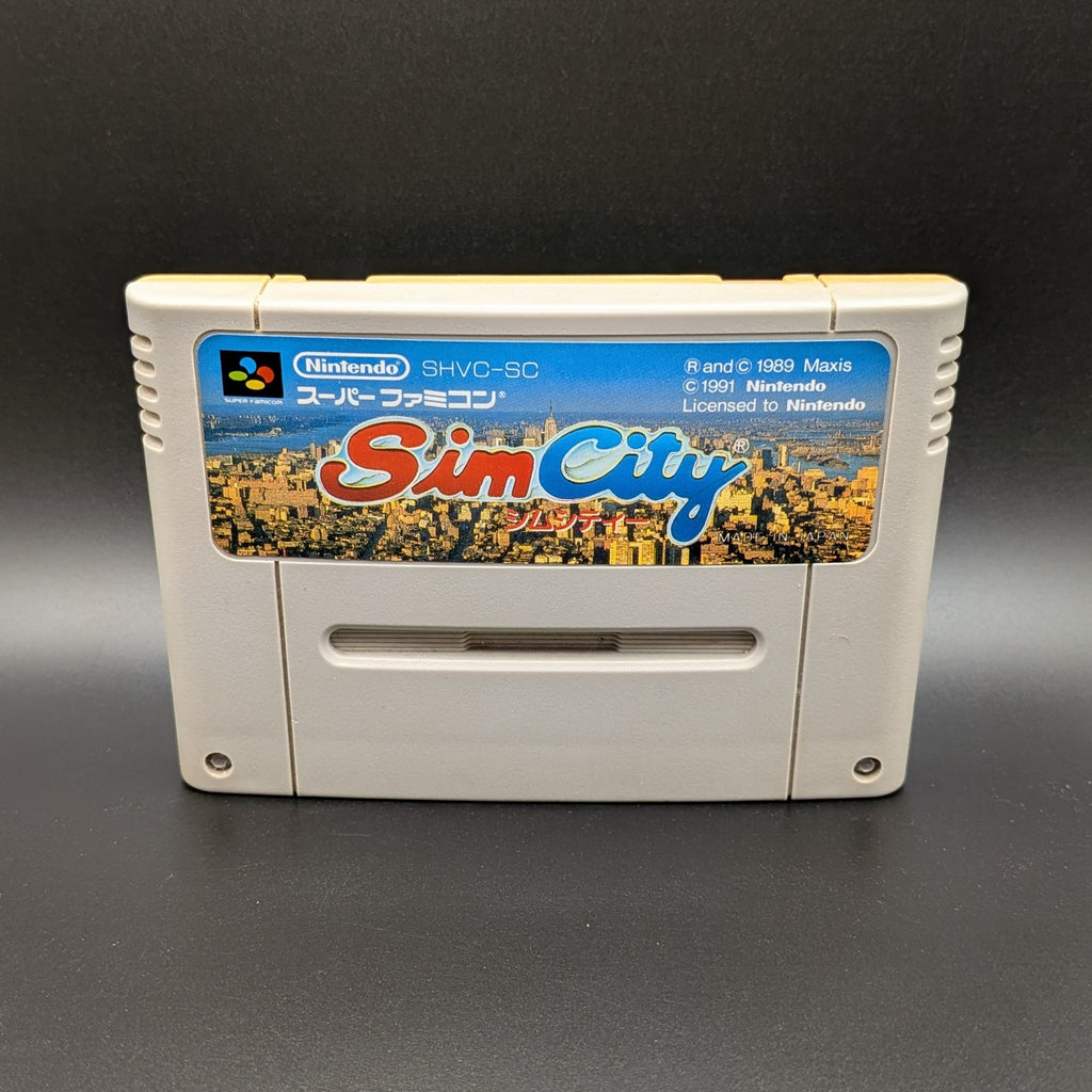 Sim City video game cartridge for Nintendo's Super Famicom (SFC) Entertainment System, shown standing up and facing forwards on a dark grey background.