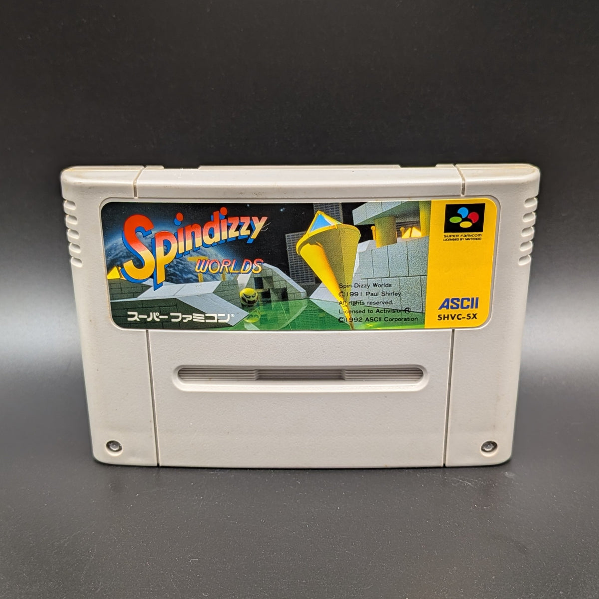 Spindizzy Worlds video game cartridge for Nintendo's Super Famicom (SFC) Entertainment System, shown standing up and facing forwards on a dark grey background.