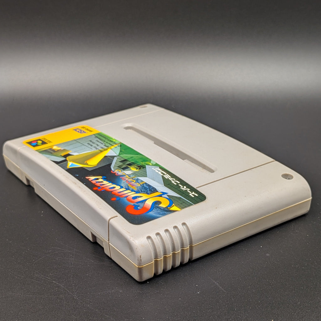 Spindizzy Worlds video game cartridge for Nintendo's Super Famicom (SFC) Entertainment System, shown laying on its back with the label facing upwards. Showing the left hand side and top edge. It sits on a dark grey background.