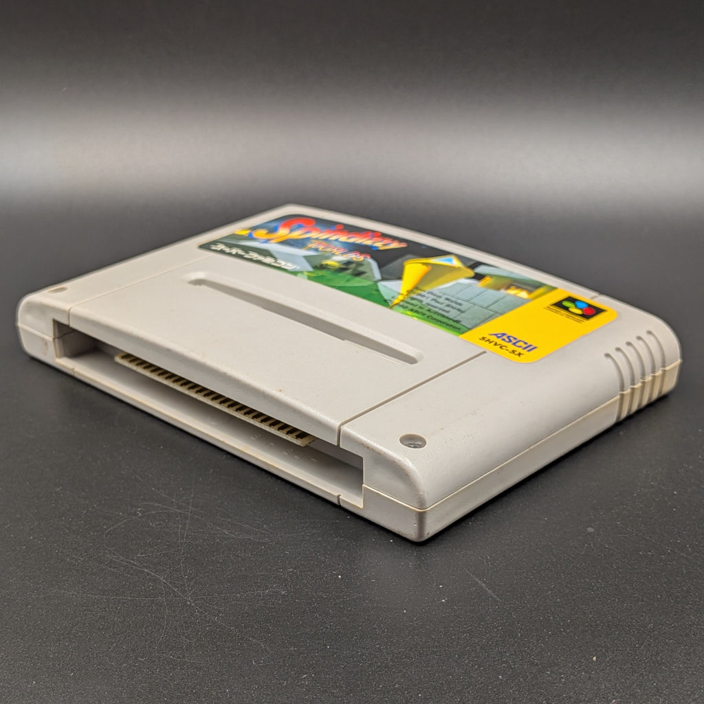 Spindizzy Worlds video game cartridge for Nintendo's Super Famicom (SFC) Entertainment System, shown laying on its back with the label facing upwards. Showing the right hand side and bottom slot. It sits on a dark grey background