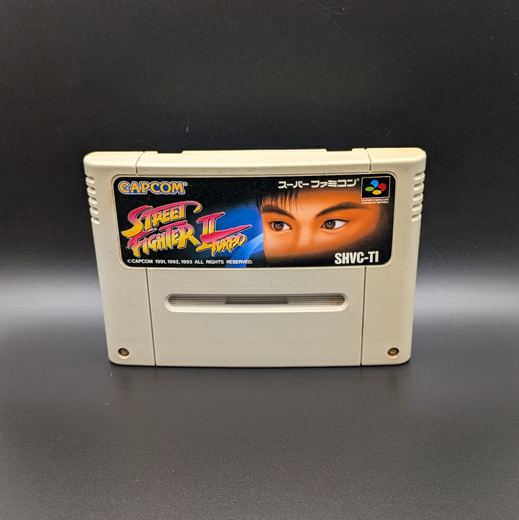 Street Fighter II Turbo: Hyper Fighting video game cartridge for Nintendo's Super Famicom (SFC) Entertainment System, shown standing up and facing forwards on a dark grey background.
