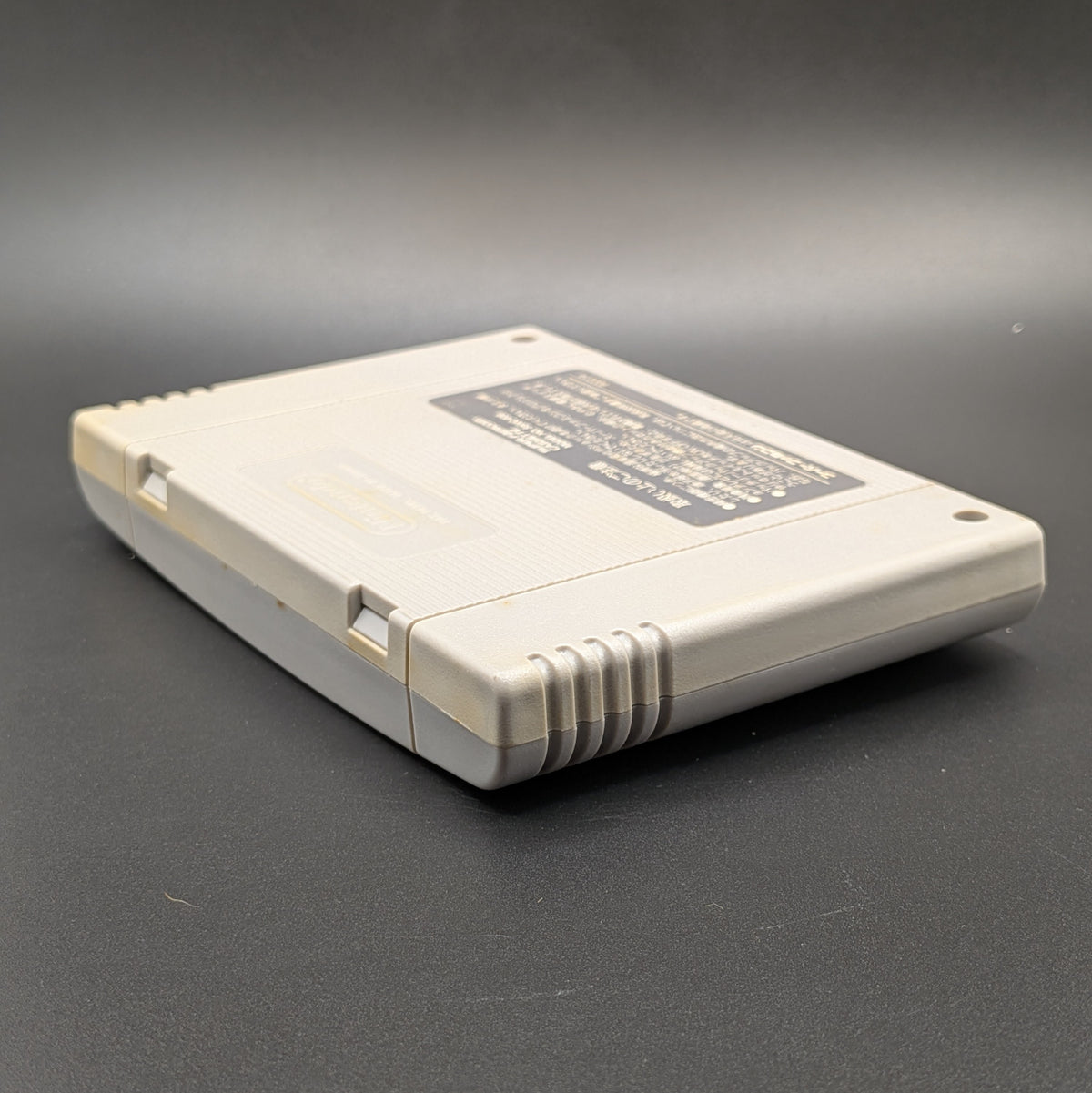 Street Fighter 2 Turbo: Hyper Fighting video game cartridge for the Super Famicom Entertainment System, shown laying on its front, at a 3/4 angle facing down so the back label is visible. Pictured on a dark grey background.