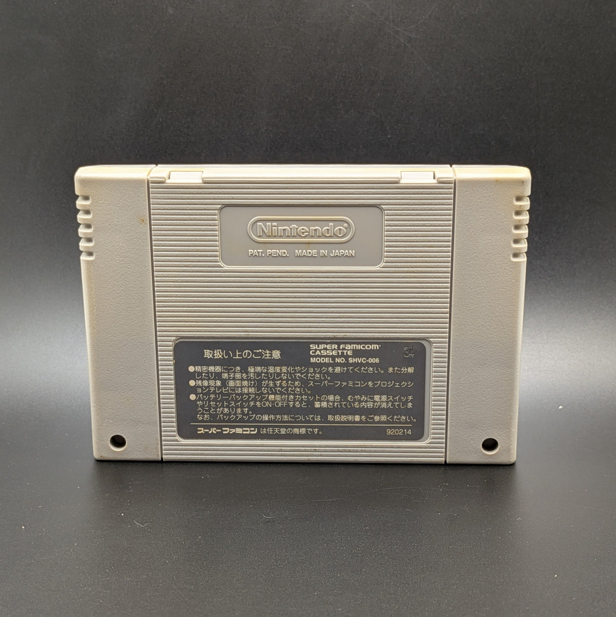 The back of the video game cartridge for  Street Fighter 2 Turbo: Hyper Fighting  for the Super Famicom. It shows the imprinted Nintendo logo and back label. Pictured on a dark grey background.