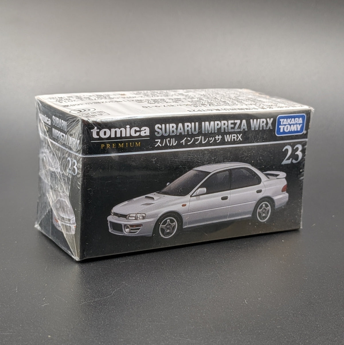 A Takara Tomy model car sealed in its packaging. This Tomica premium model shows a Subaru Impreza WRX on the front of the packaging which is sat on a dark grey background.