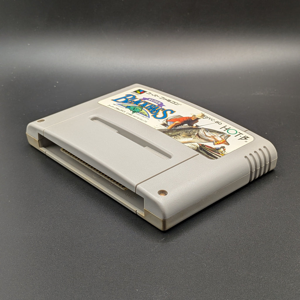 Super Black Bass video game cartridge for Nintendo's Super Famicom (SFC) Entertainment System, shown  laying on its back at a 3/4 view on a dark grey background.
