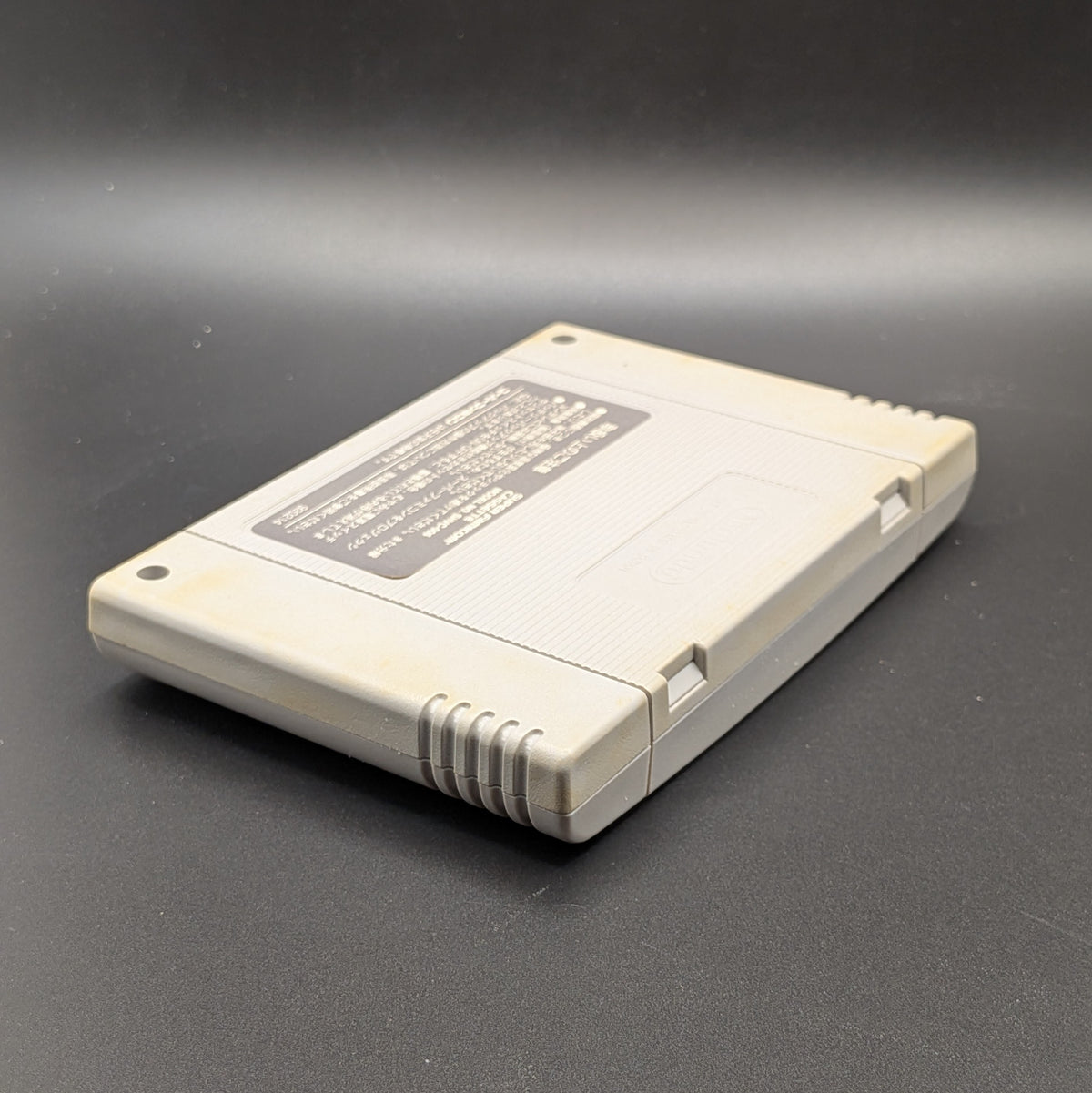 Super Black Bass video game cartridge for Nintendo's Super Famicom (SFC) Entertainment System, shown laying on its front, back label and logo visible at a 3/4 view, on a dark grey background.