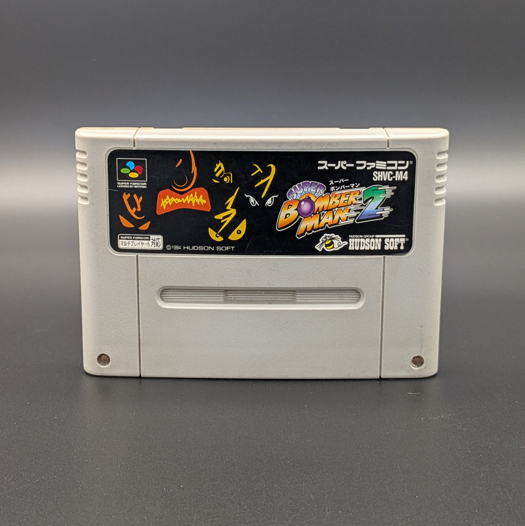Super Bomberman 2 video game cartridge for Nintendo's Super Famicom (SFC) Entertainment System, shown standing up and facing forwards on a dark grey background.