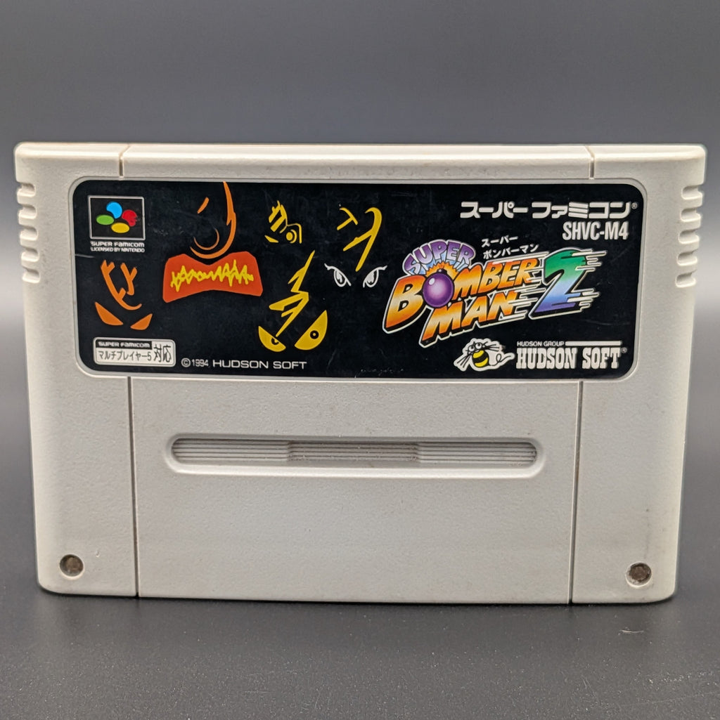 A close up of Super Bomberman 2 video game cartridge for Nintendo's Super Famicom (SFC) Entertainment System, shown standing up and facing forwards on a dark grey background.