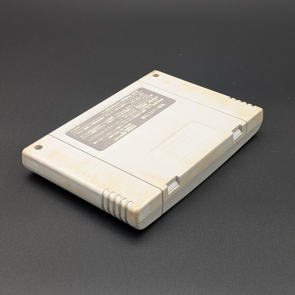Super Bomberman 2 video game cartridge for Nintendo's Super Famicom (SFC) Entertainment System, shown laying on its face with the back label facing upwards. Showing the right hand side and top edge. It is displayed on a dark grey background.