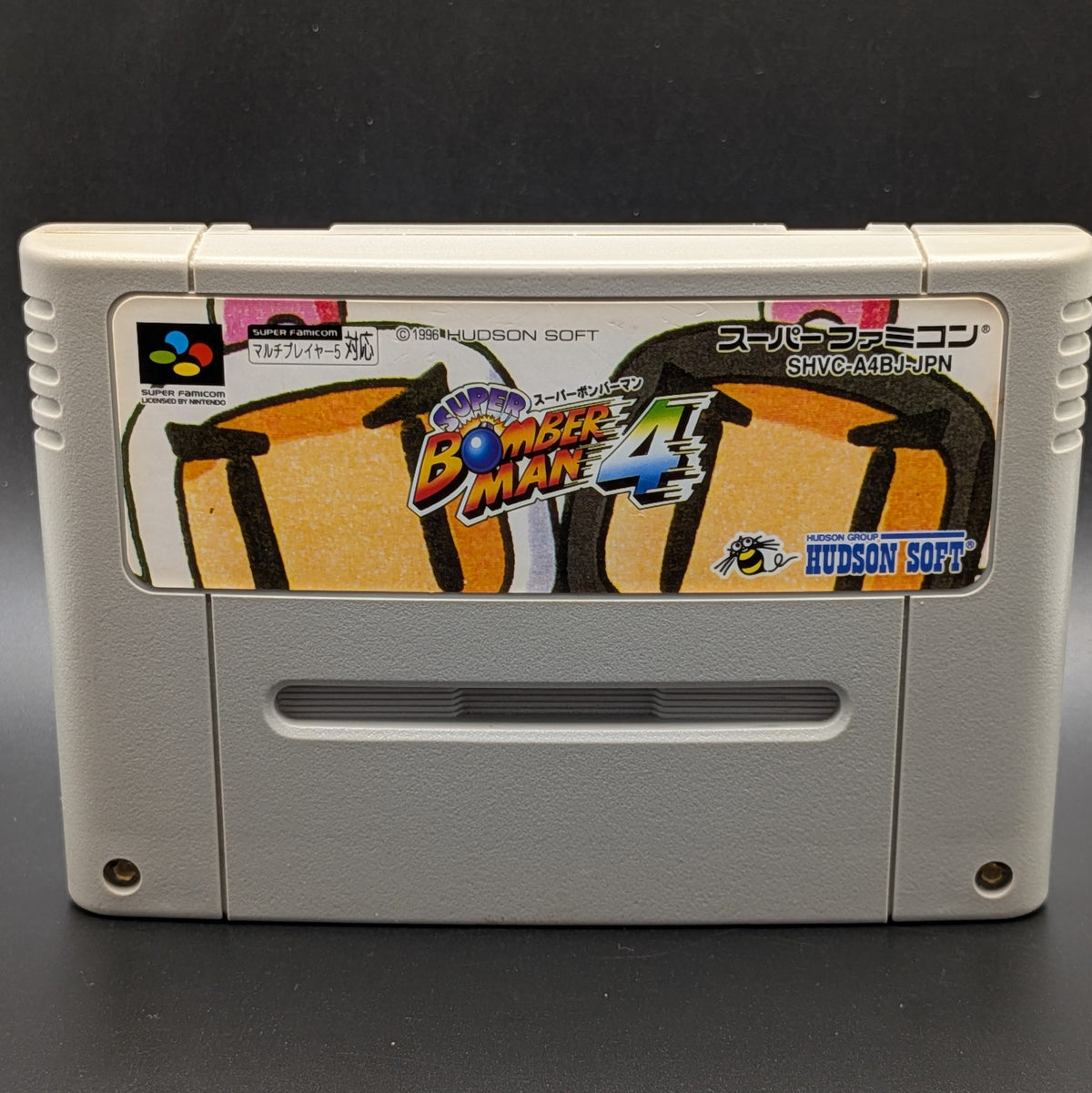 a close up of Super Bomberman 4 video game cartridge for Nintendo's Super Famicom (SFC) Entertainment System, shown standing up and facing forward on a dark grey background.
