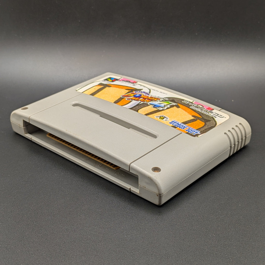 Super Bomberman 4 video game cartridge for Nintendo's Super Famicom (SFC) Entertainment System, shown laying on its back with the label facing upwards. It sits on a dark grey background.
