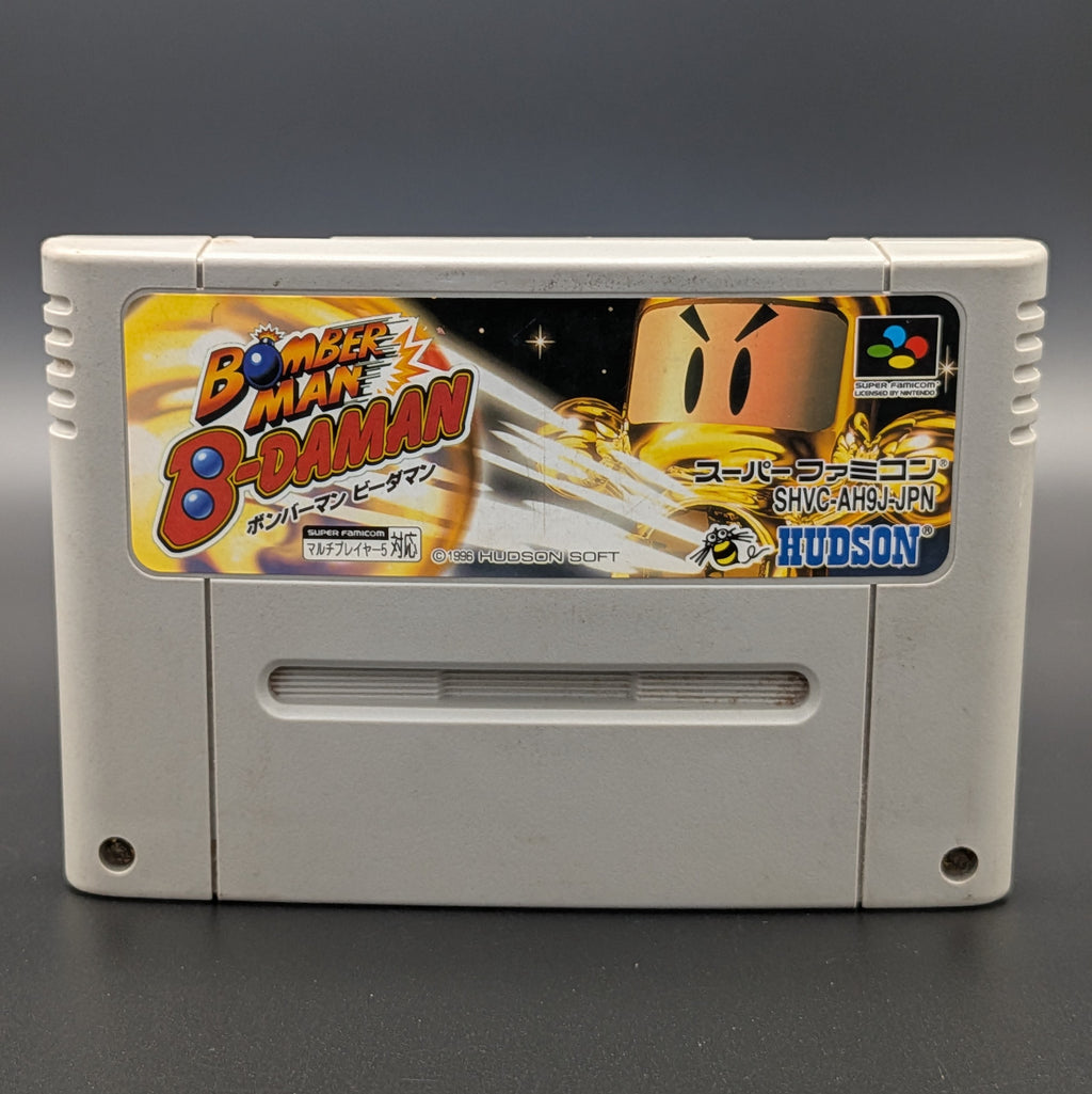A close up of Super Bomberman B-Daman video game cartridge for Nintendo's Super Famicom (SFC) Entertainment System, shown standing up and facing forward on a dark grey background.
