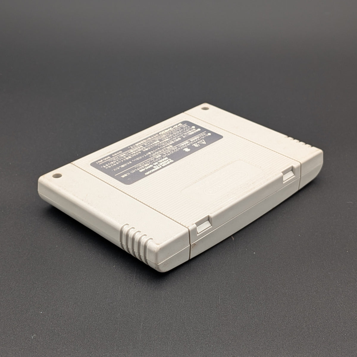 Super Bomberman B-Daman video game cartridge for Nintendo's Super Famicom (SFC) Entertainment System, shown laying on its front, showing the back label. It sits on a dark grey background.


