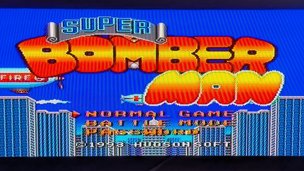 The game title screen of the video game Super BomberMan, showing large red-to-yellow gradient title text over a bright blue background with city buildings and menu options. Released on the Super Famicom (SFC) by Nintendo.